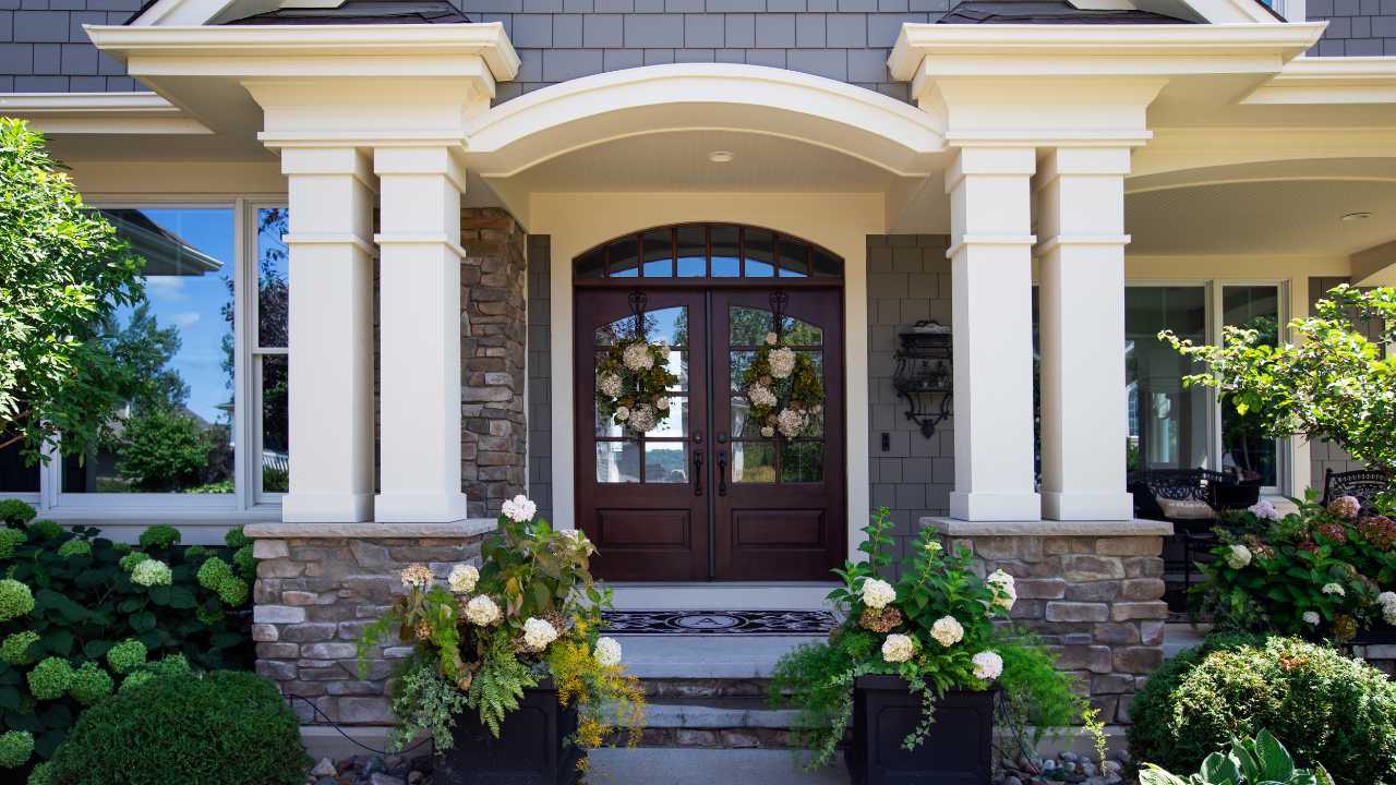Dark Wooded Door Leading to House with Wreaths On Top and White Archway