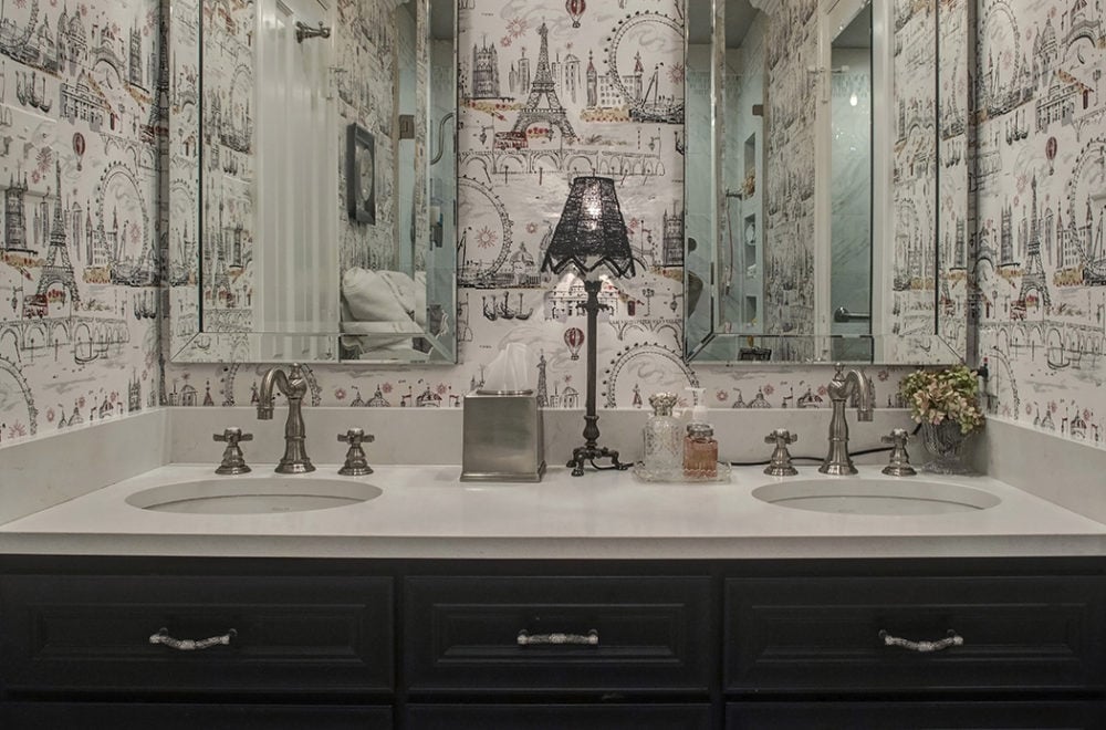Bathroom with Busy Wallpaper and Lamp on Sink Between Two Mirrors on Counter