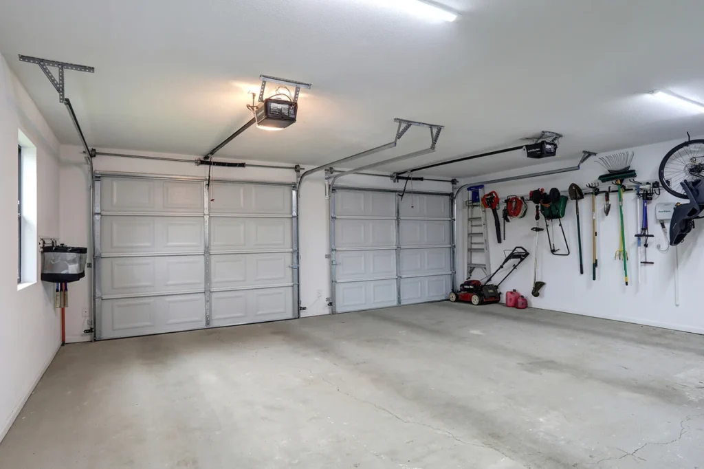 A clean, empty garage with two closed doors, a wall-mounted sink, and organized tools and equipment hanging on the right wall.