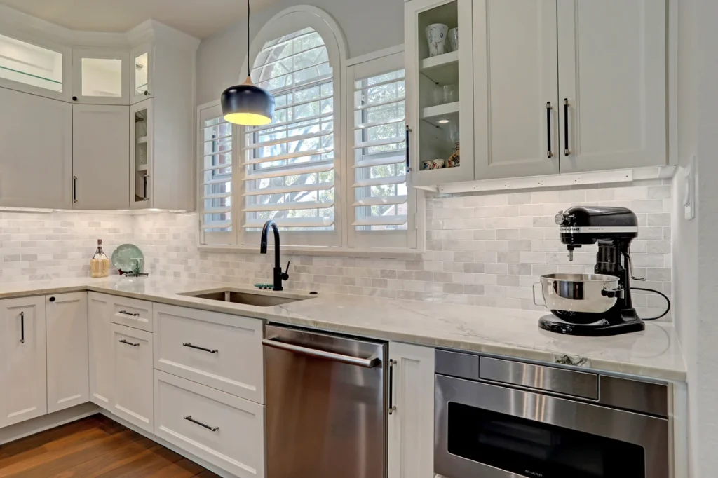 Modern kitchen with white cabinets, stainless steel appliances, a stand mixer, a large sink, and a window with shutters above the countertop.