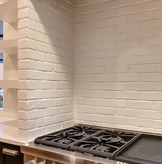 A stainless steel gas stove with four burners is set against a white painted brick backsplash in a modern kitchen.