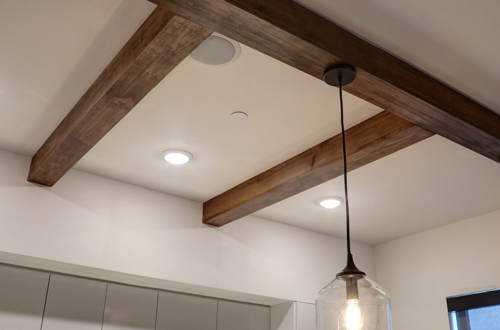 Ceiling with exposed wooden beams, recessed lighting, a round ceiling speaker, and a hanging glass pendant light.