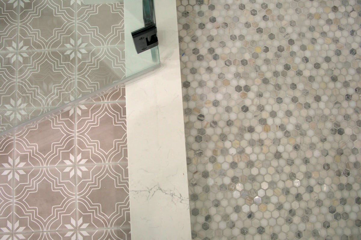 Marble divider separates two floor patterns: one side has beige geometric tiles, the other side has small hexagonal mosaic tiles in neutral tones.