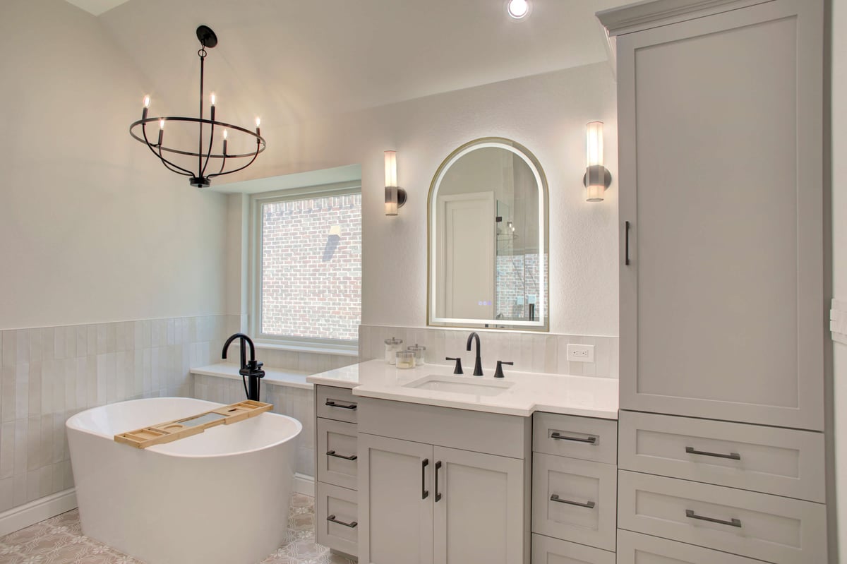 Modern bathroom with a white freestanding tub, black fixtures, a double-sink vanity, arched mirror, and pendant lighting near a window.