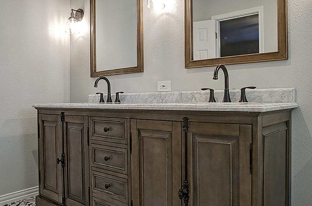 Double bathroom vanity with marble countertop, two sinks, two mirrors, bronze fixtures, and wooden cabinets in a neutral-toned bathroom.