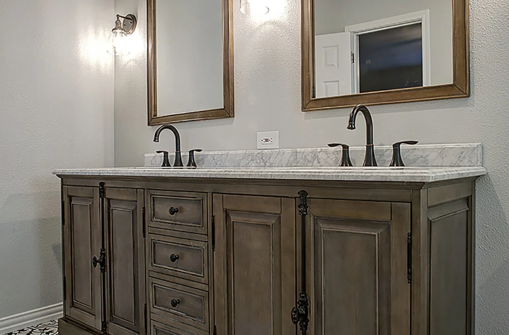 A double bathroom vanity with a marble countertop, two sinks, bronze fixtures, two mirrors, and a wooden cabinet base.