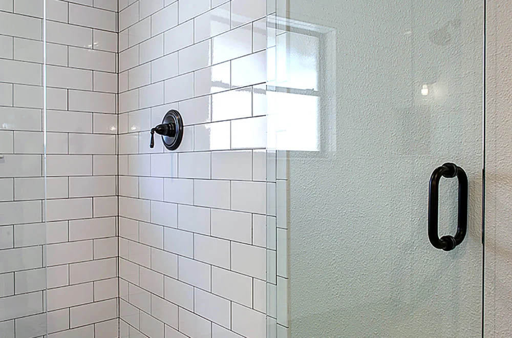 Shower with white subway tile walls, black metal fixtures, and a glass door with a black handle.