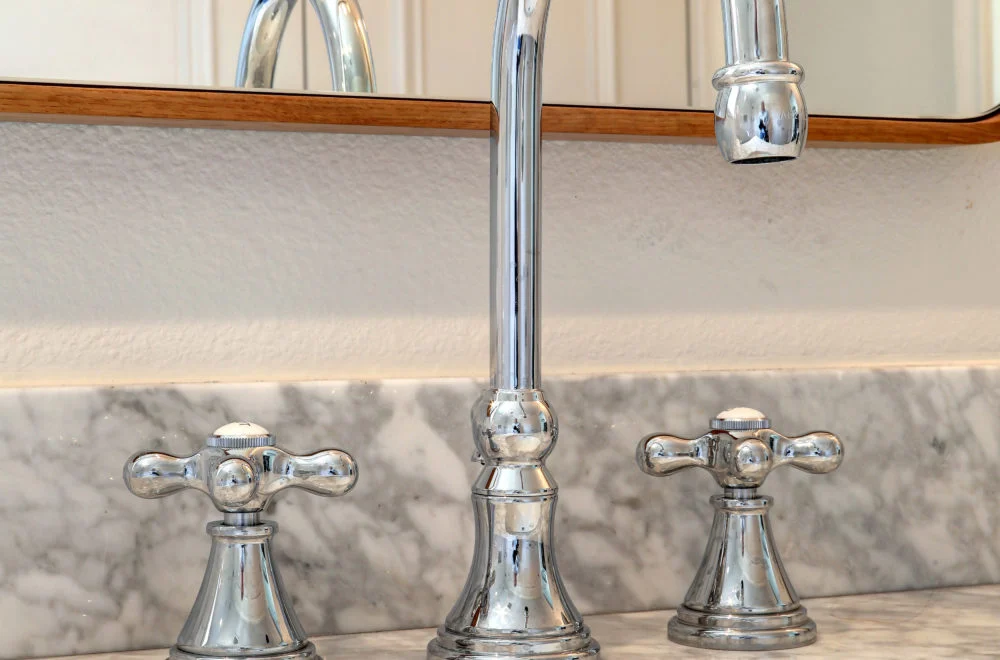 Close-up of a silver bathroom faucet with separate hot and cold handles on a marble countertop, with a mirror in the background.