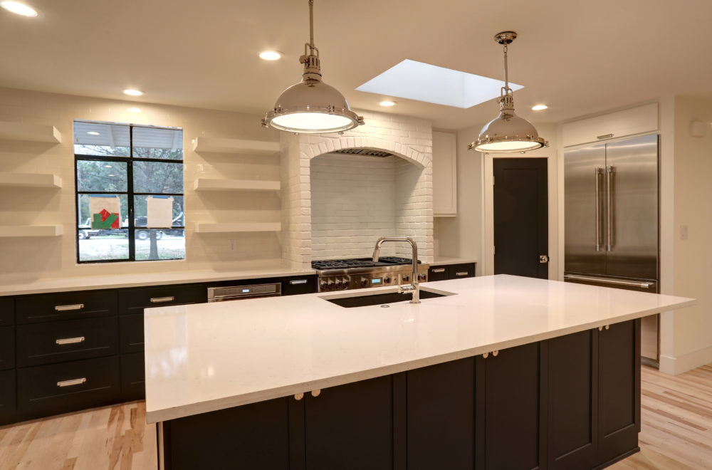 Modern kitchen with a large white island, dark cabinetry, stainless steel appliances, open shelves, pendant lighting, and a window above the sink.
