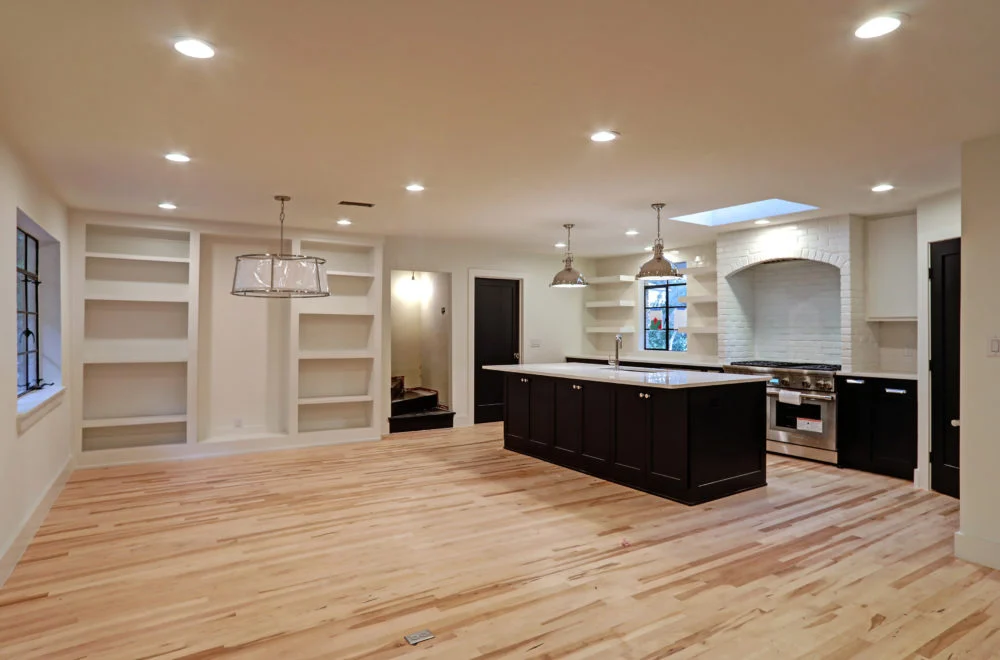 Modern open-concept kitchen and living area with built-in shelves, light wood flooring, and a large island with pendant lighting.