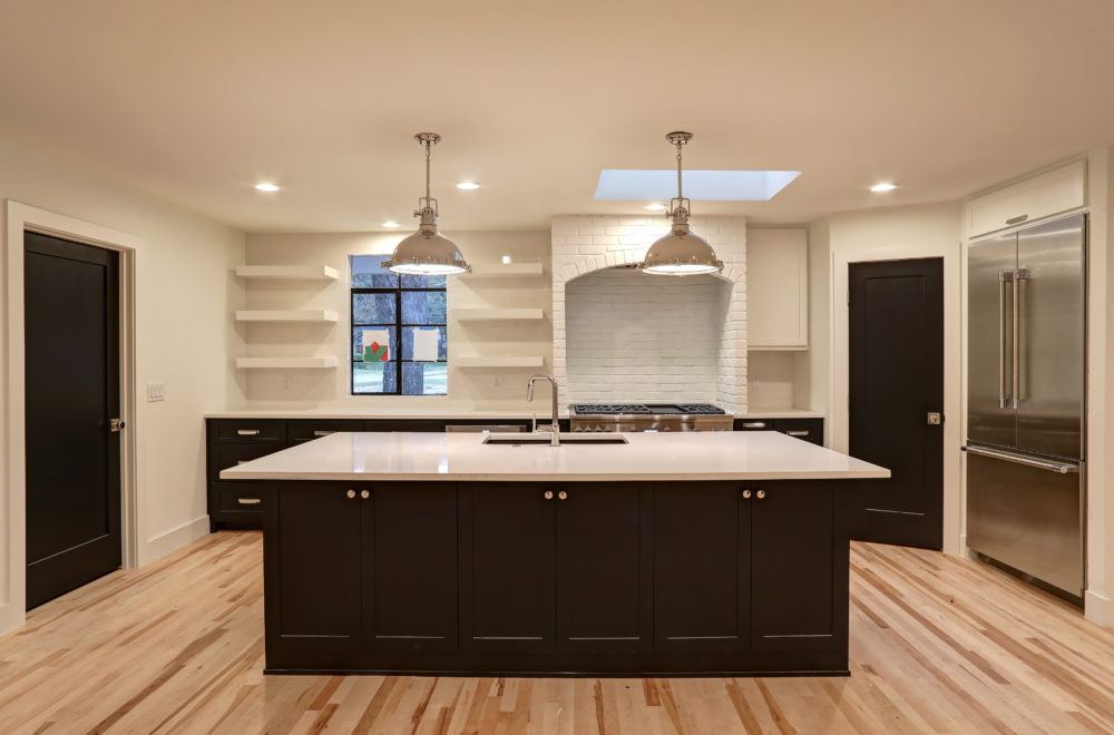 Modern kitchen with a large island, pendant lights, stainless steel appliances, open shelves, white brick backsplash, and light wood floors.