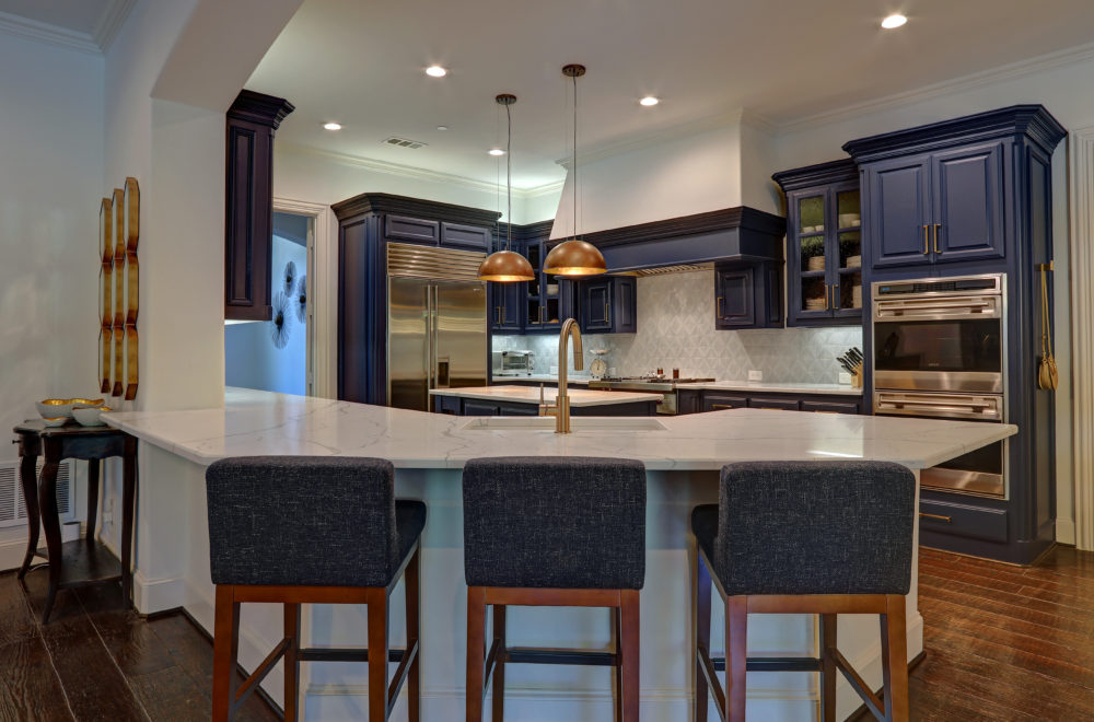 Modern kitchen with navy cabinets, stainless steel appliances, marble countertop, three dark barstools, and two pendant lights above the island.