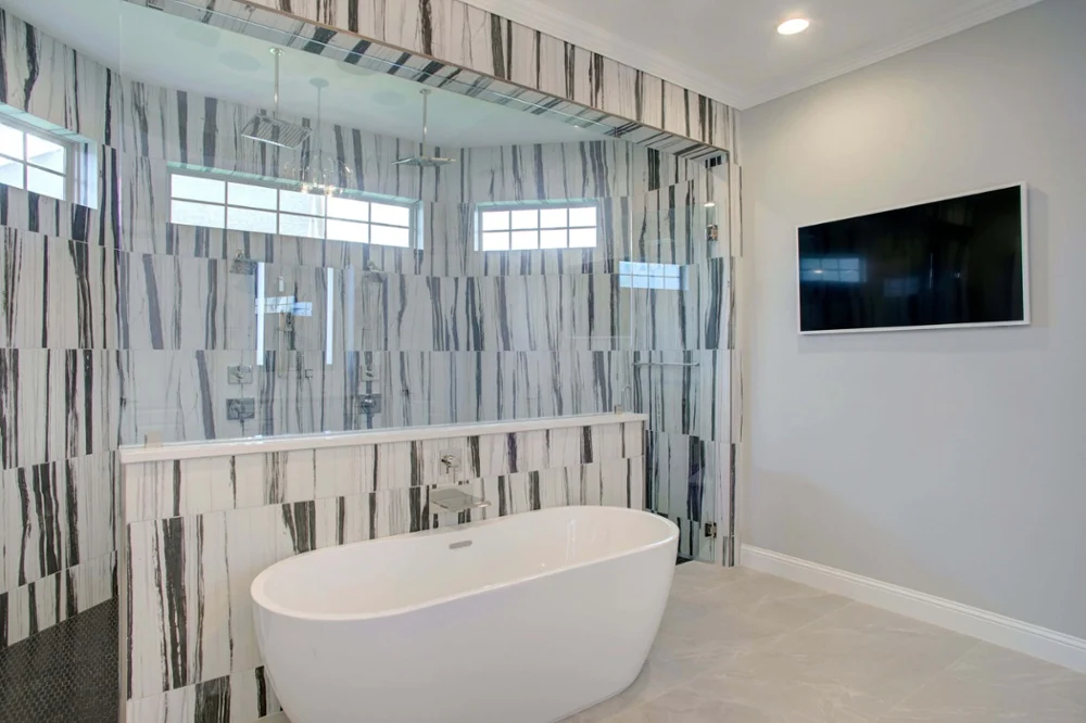 Modern bathroom with a freestanding white bathtub, a large glass-enclosed shower with vertical striped tiles, and a wall-mounted flat-screen TV.