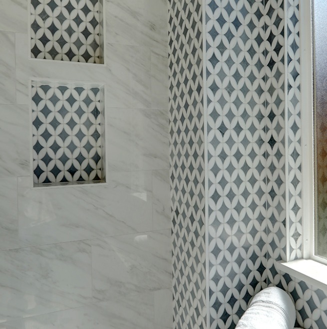Shower wall with white marble tiles, two recessed niches, and an accent wall featuring a geometric pattern in gray and white next to a frosted window.