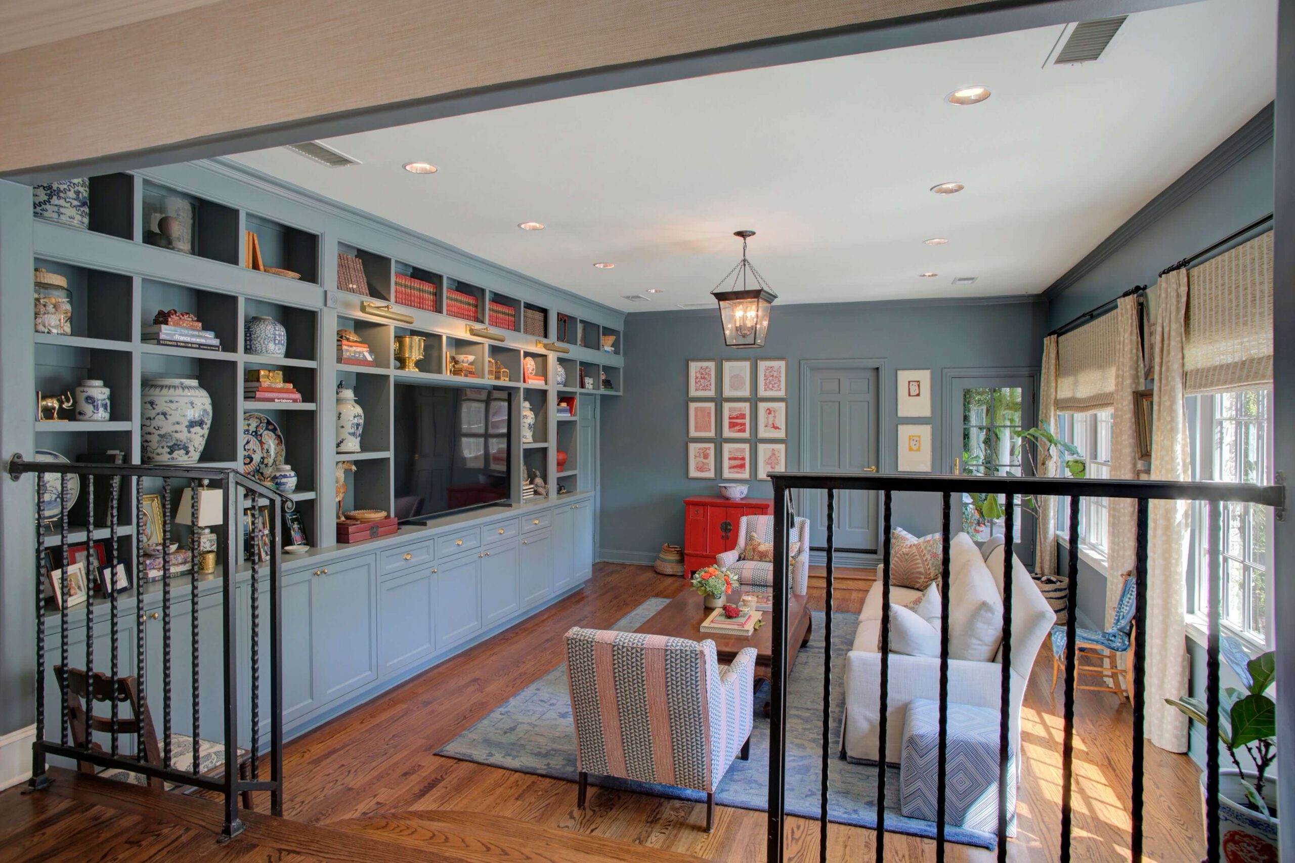 A living room with blue built-in shelves, decorative vases, a sofa, armchairs, a coffee table, hardwood floors, and large windows with natural light.