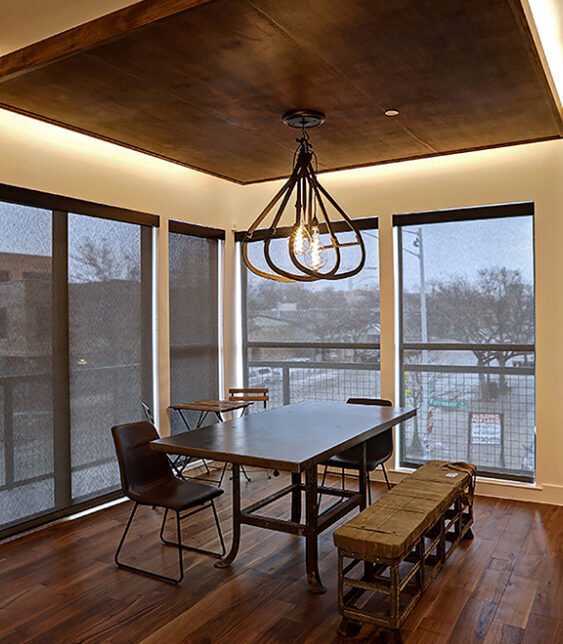loft-dining-1000x660 Modern dining area with industrial-style metal table, mismatched chairs, a wooden bench, large windows with blinds, and a geometric pendant light fixture overhead.