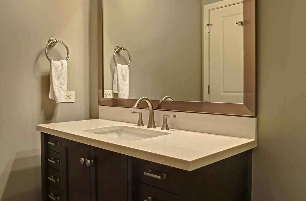 Modern bathroom vanity with a rectangular sink, stainless steel faucet, dark wood cabinets, large mirror, and a towel hanging on a ring to the left.
