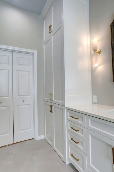 White built-in cabinets with gold handles next to a double door closet, under a wall-mounted light fixture, in a modern interior space.
