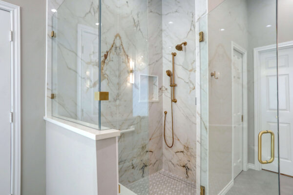 Glass-enclosed shower with marble tile walls, gold shower fixtures, and a built-in niche.