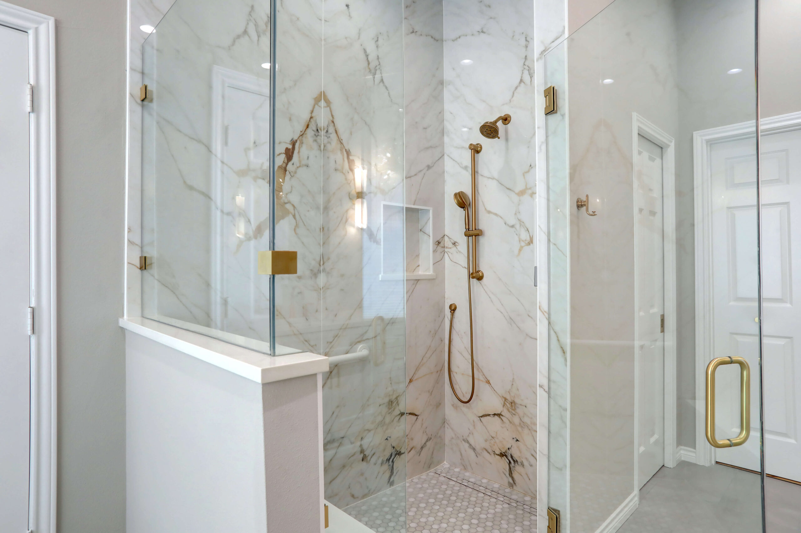 Glass-enclosed shower with marble tile walls, gold shower fixtures, and a built-in niche.