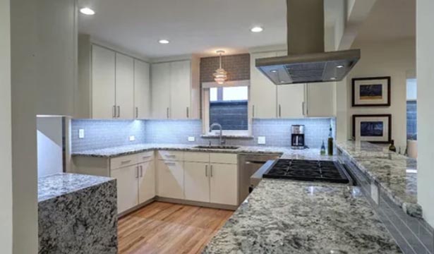 Modern kitchen with white cabinets, granite countertops, stainless steel appliances, under-cabinet lighting, and hardwood floors.