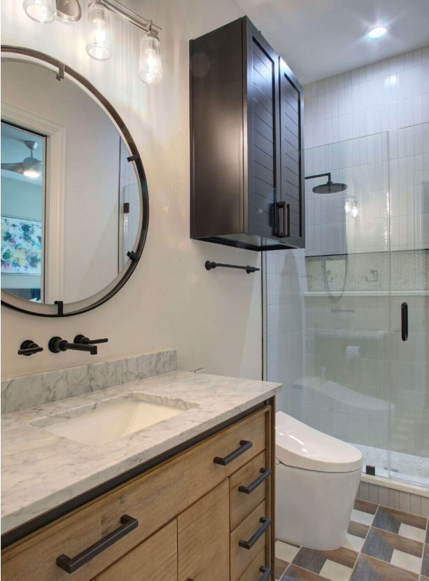 Modern bathroom with a marble countertop, round mirror, black fixtures, wall-mounted cabinet, and glass-enclosed shower.