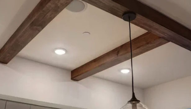 Ceiling with two wooden beams, recessed lights, a circular ceiling speaker, and a hanging pendant light fixture.