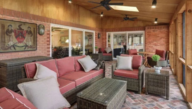 Screened-in porch with wicker furniture featuring red cushions, a brick wall, ceiling fans, a skylight, and decorative artwork on the wall.